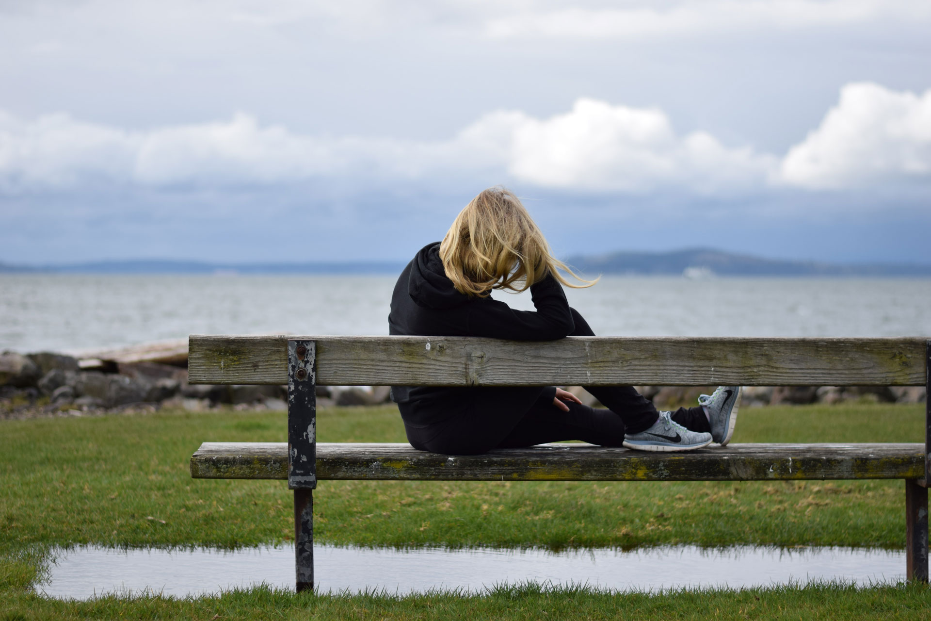 Woman sitting on a park bench looking out at the ocean.